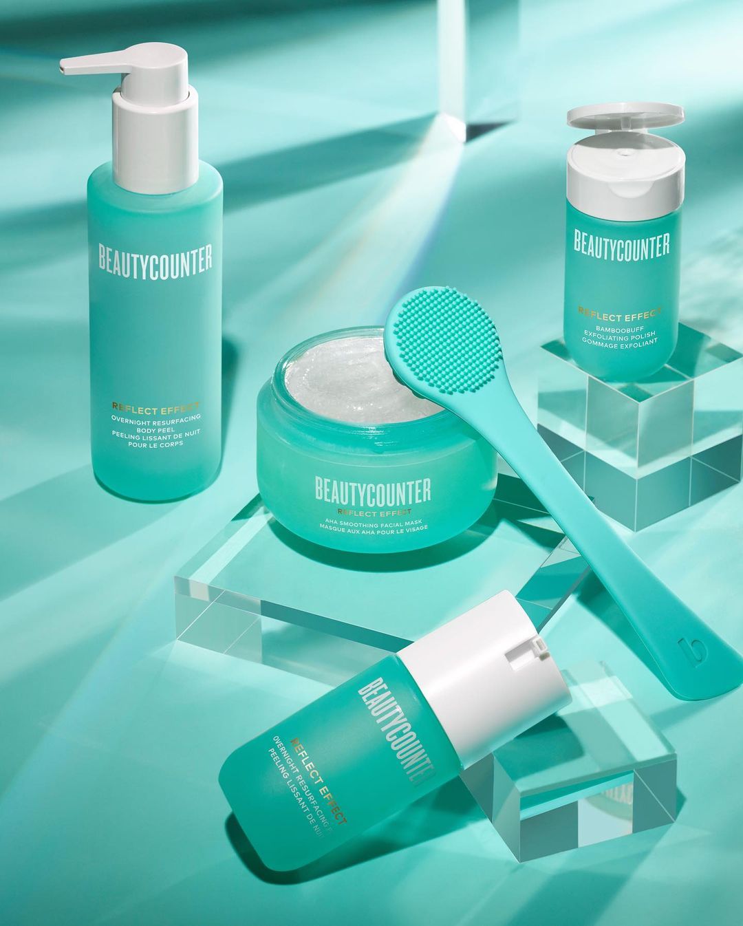 Beautycounter skincare products including cleanser, body butter, and a facial mask arranged on clear acrylic blocks in studio setting.