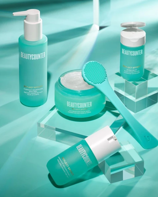 Beautycounter skincare products including cleanser, body butter, and a facial mask arranged on clear acrylic blocks in studio setting.