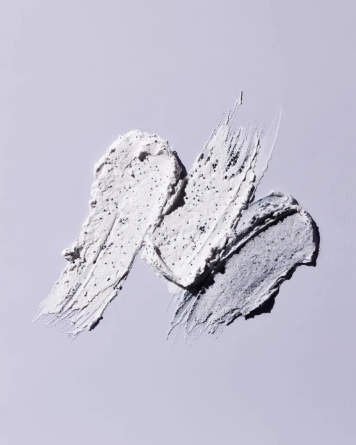 Three swipes of cream with scrub granules on a light purple surface. Cosmetic product shot for beauty, skincare, or health.