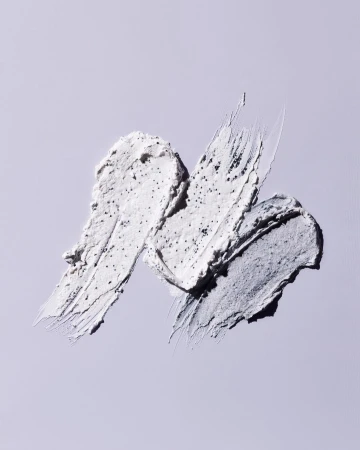 Three swipes of cream with scrub granules on a light purple surface. Cosmetic product shot for beauty, skincare, or health.
