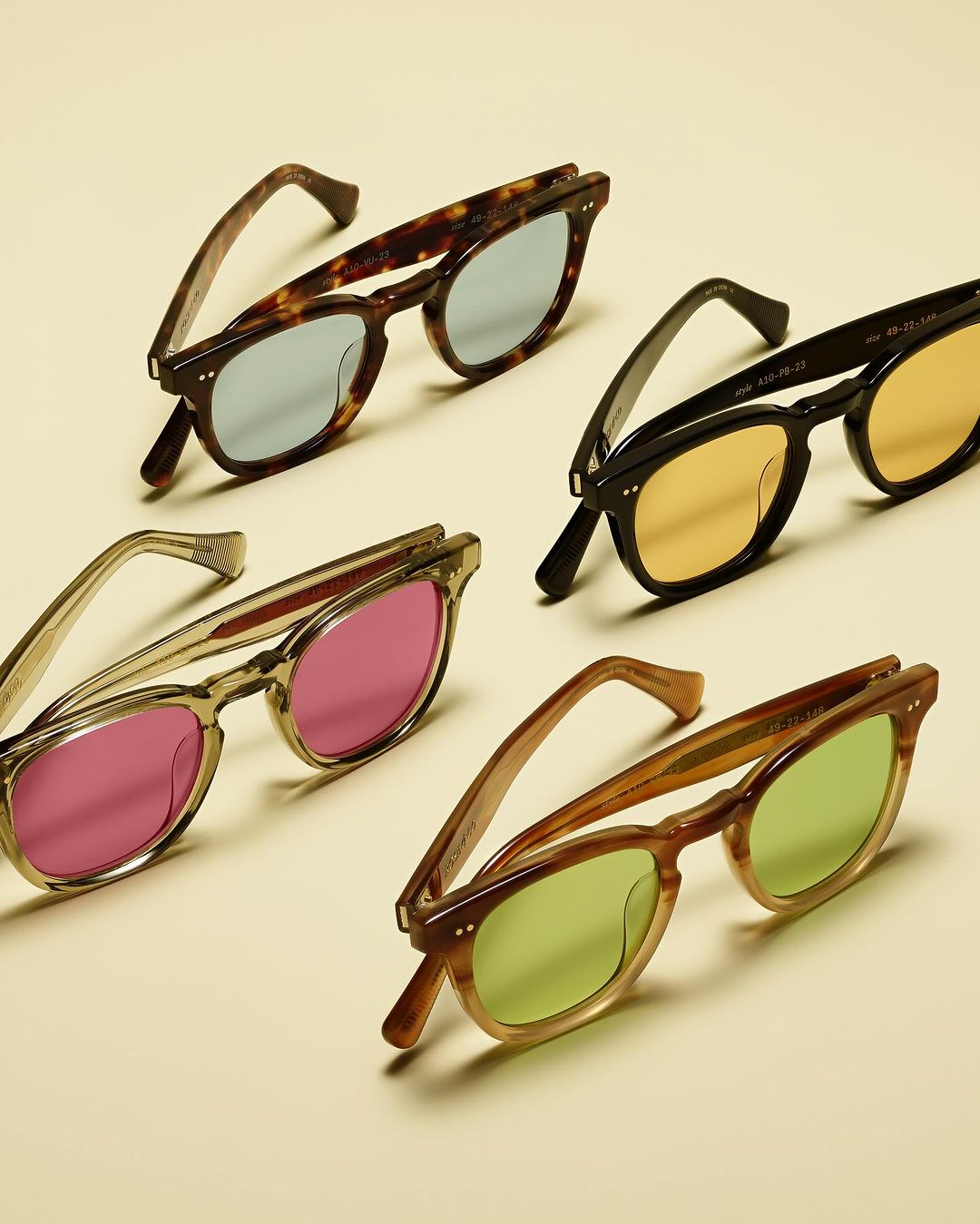 Four pairs of colorful sunglasses are neatly arranged on a cream-colored surface in a product shot, exhibiting style and design.