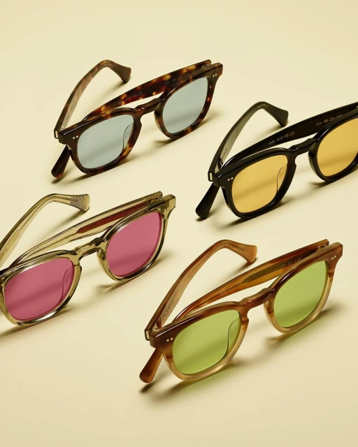 Four pairs of colorful sunglasses are neatly arranged on a cream-colored surface in a product shot, exhibiting style and design.