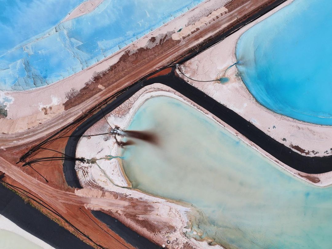 Aerial view of colorful salt ponds and industrial infrastructure, featuring striking turquoise waters and earthy brown banks.