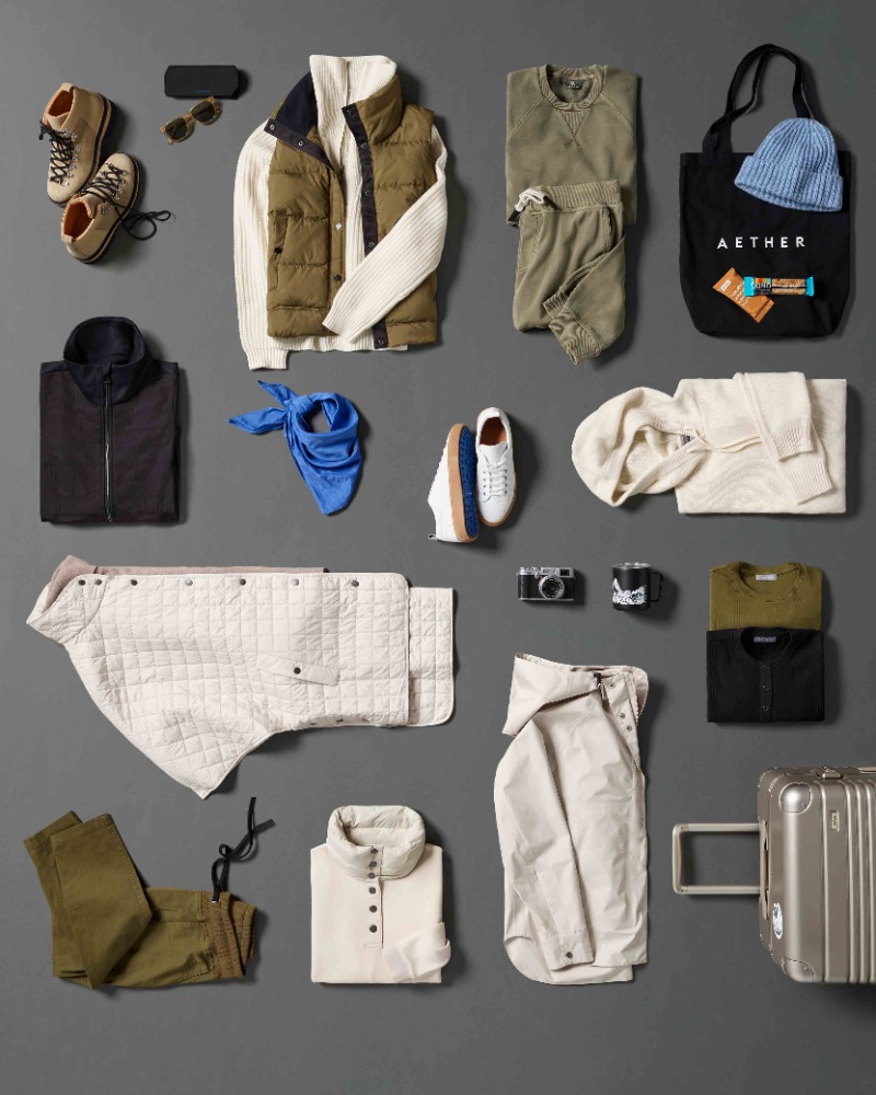 Flat lay of a curated selection of clothing and accessories in neutral tones, arranged on a gray background for a lifestyle product display.
