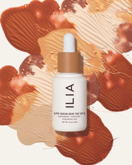 Ilia Super Serum Skin Tint SPF 30 product shot on a neutral surface with terracotta and tan color swatches in the background.
