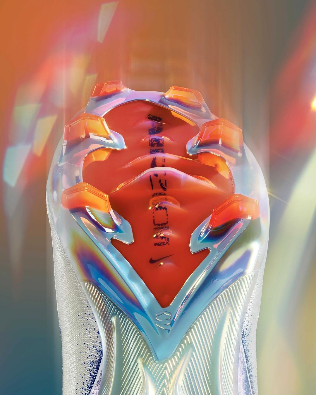 Close-up of the sole of a Nike soccer cleat featuring the word Zoom and an iridescent appearance against a soft gradient background.