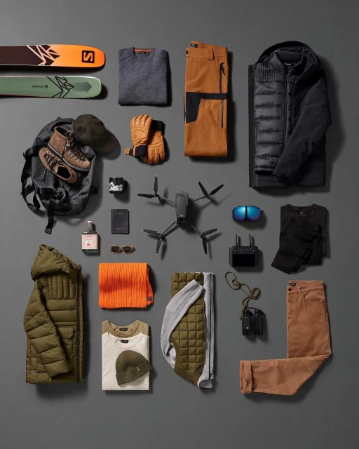 Overhead shot of organized outdoor gear: skis, drone, clothing, and accessories laid out on a grey surface for a flat lay composition.