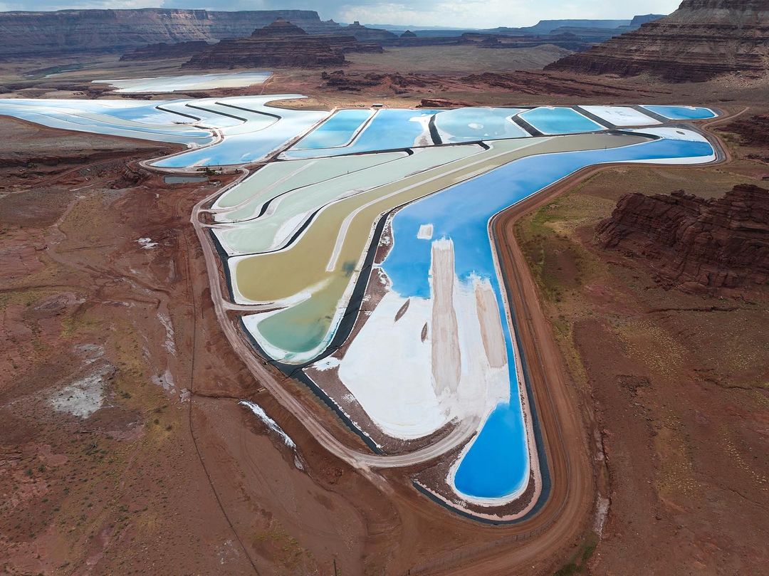 Aerial landscape of potash evaporation ponds in Moab, Utah with terraced colorful pools, mountains and canyons on a cloudy day.