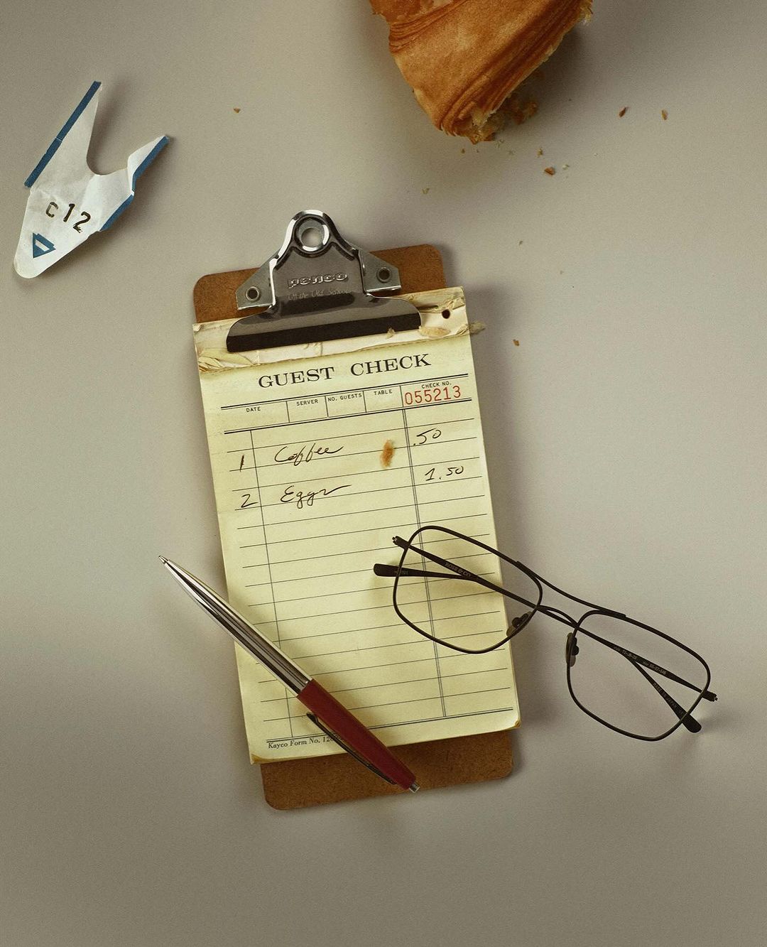 Overhead shot of a cafe order ticket, pen, glasses, and pastry on a light gray surface, perfect for a food and beverage concept.