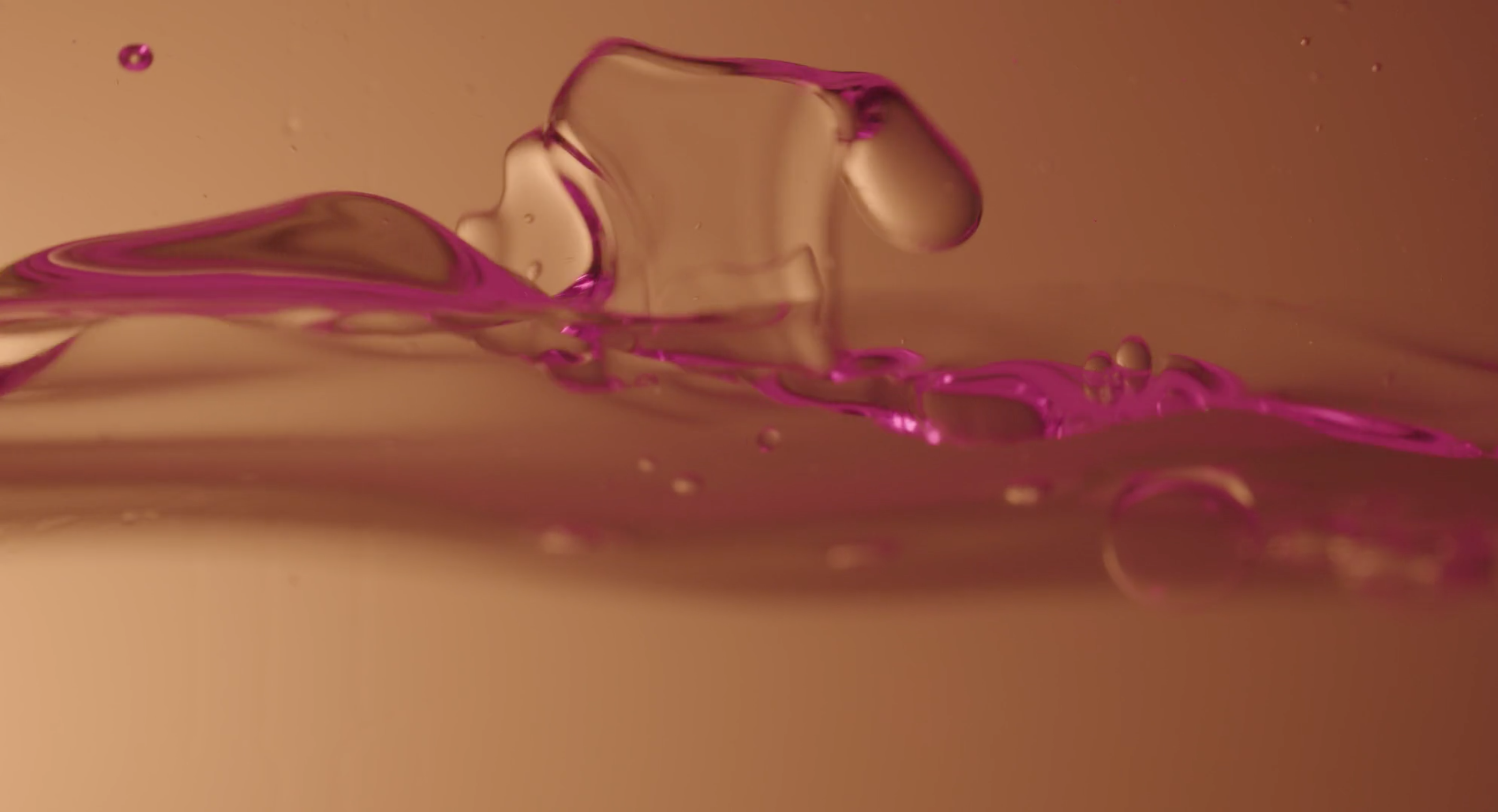 Abstract close-up of water with a purple edge and droplets, set against a warm-toned background, creating a dynamic liquid texture.