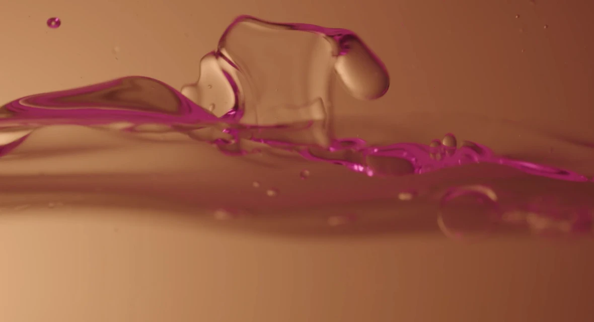 Abstract close-up of water with a purple edge and droplets, set against a warm-toned background, creating a dynamic liquid texture.