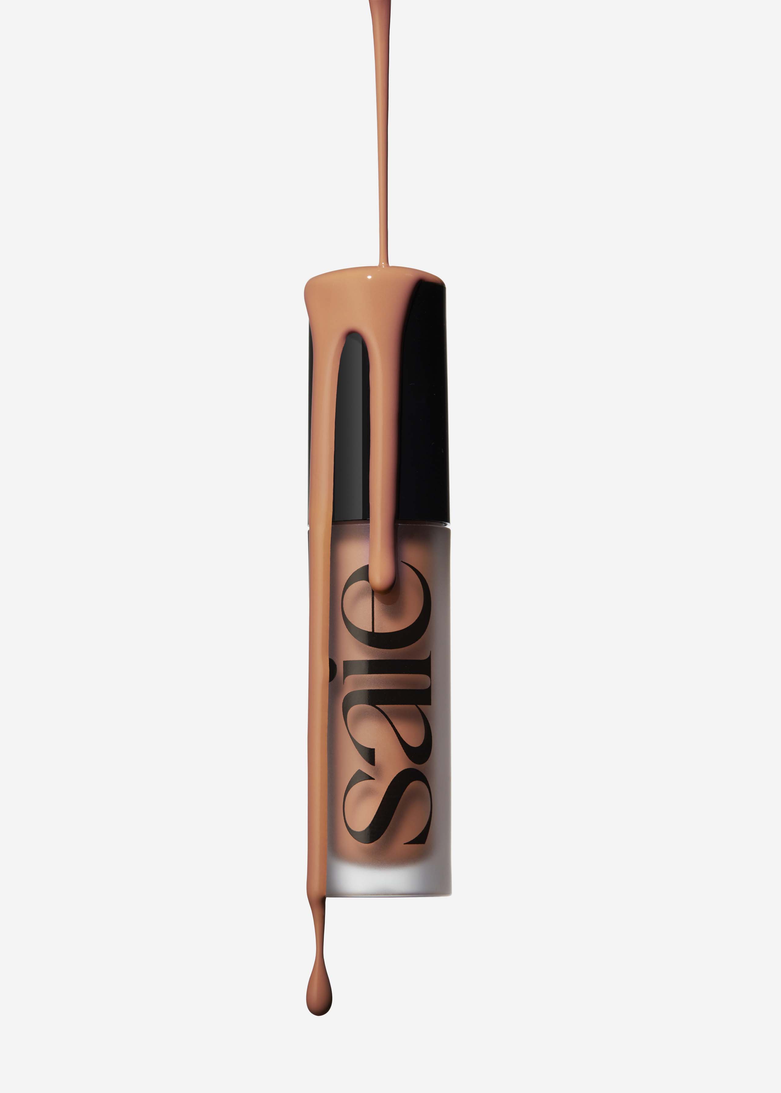 Foundation makeup product with peach-colored liquid dripping on it, against a bright white background in a studio setting.