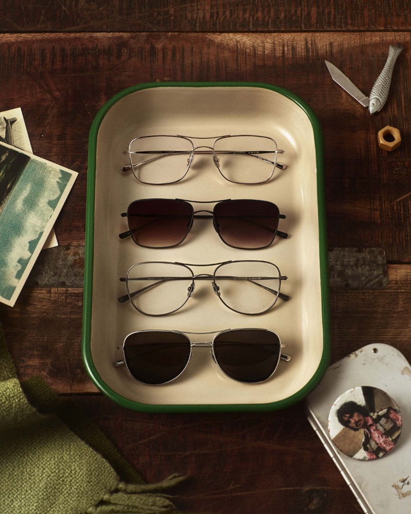 Four pairs of eyeglasses and sunglasses arranged vertically inside a white and green enameled metal tray on a wooden surface.