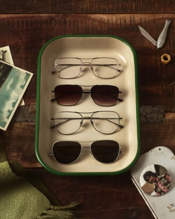 Four pairs of eyeglasses and sunglasses arranged vertically inside a white and green enameled metal tray on a wooden surface.
