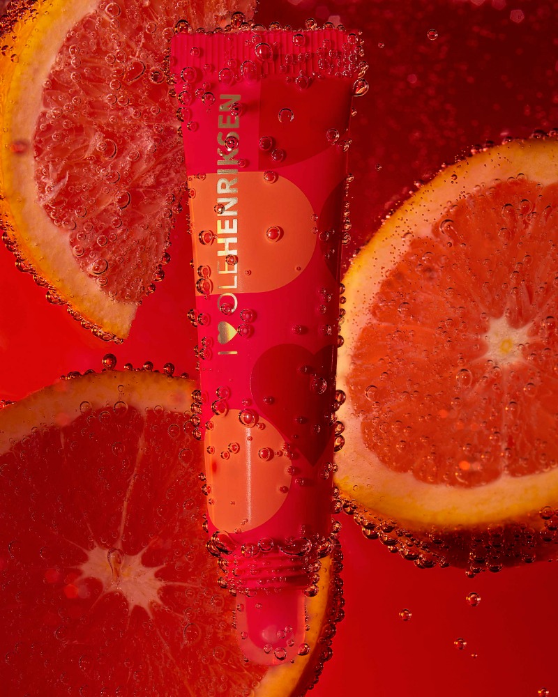Ole Henriksen skincare product tube surrounded by orange slices and bubbles in a red liquid backdrop with refreshing composition.