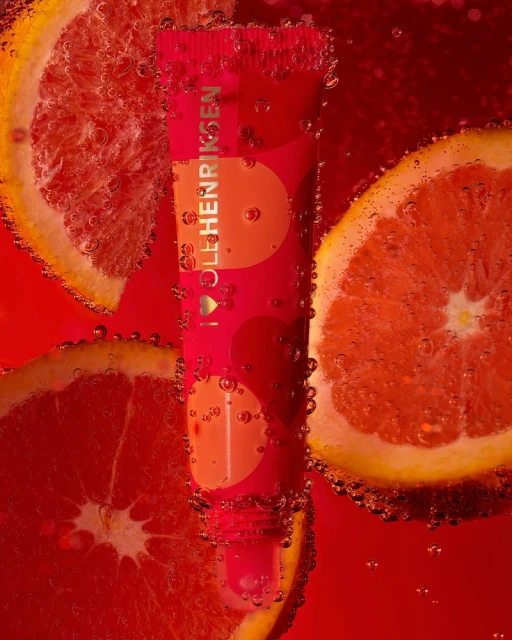Ole Henriksen skincare product tube surrounded by orange slices and bubbles in a red liquid backdrop with refreshing composition.