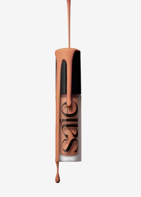 Cosmetic product bottle with peach-colored liquid dripping down, set against a clean white backdrop in a beauty product shot.
