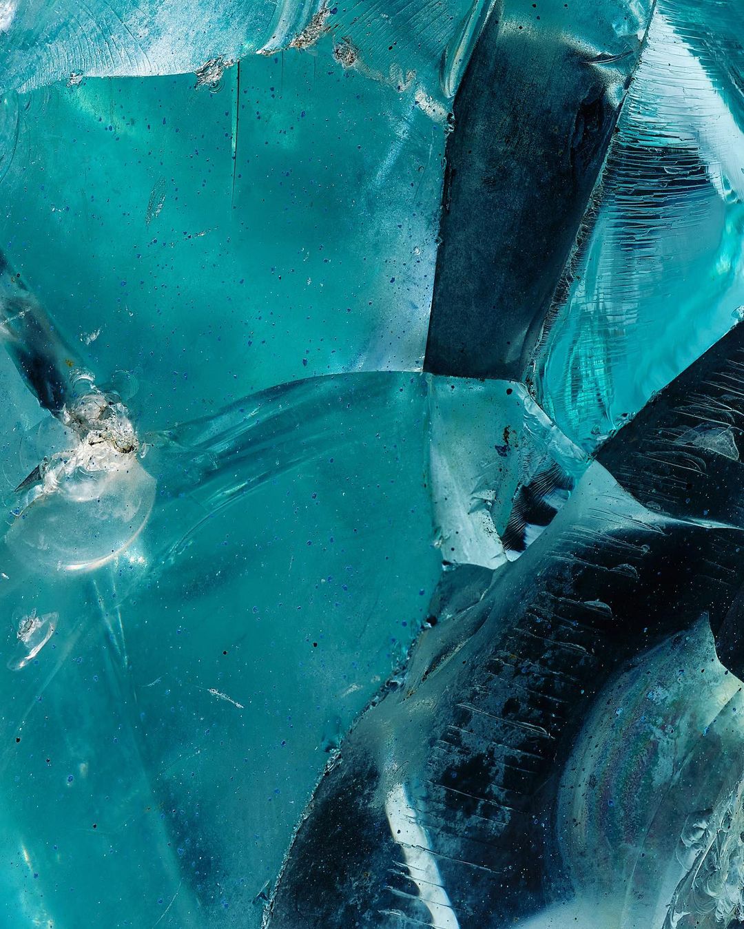 Macro image featuring fractured shards of translucent cyan glass, showcasing sharp edges, crystalline patterns, and light refraction.