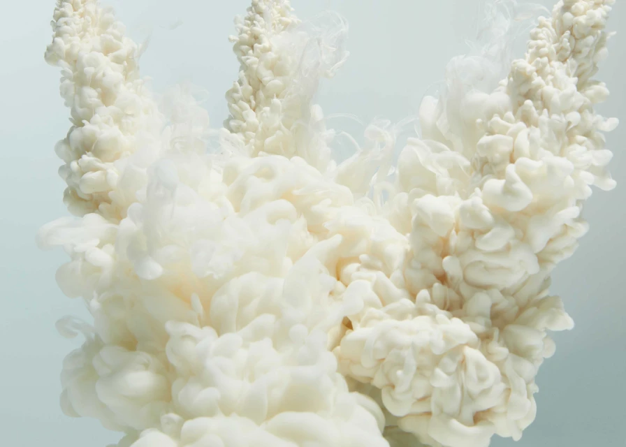 Abstract view of dense white liquid with wisps and peaks against a gradient light blue background in a studio photography setting.