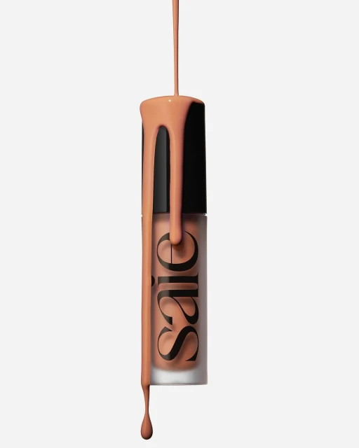 Foundation makeup in a glass bottle with a black cap and product dripping down against a white background in a studio shot.