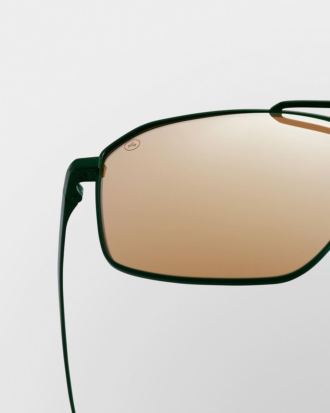 Close-up of sleek, green-framed sunglasses with amber lenses against a clean, bright background, highlighting eyewear fashion.