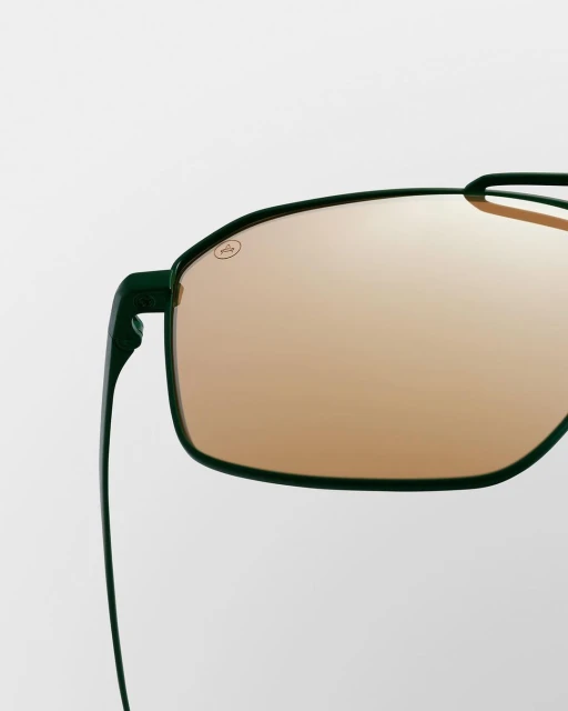 Close-up of sleek, green-framed sunglasses with amber lenses against a clean, bright background, highlighting eyewear fashion.