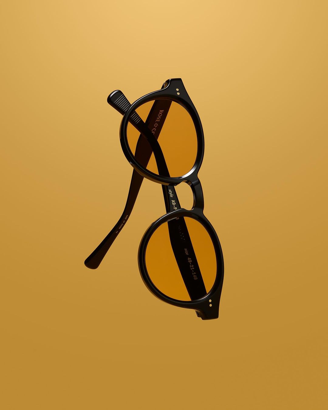 Black round sunglasses with orange lenses on an golden background. Stylish eyewear product shot. Fashion accessory studio image.