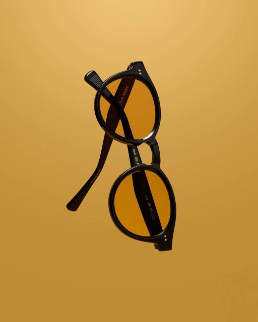 Black round sunglasses with orange lenses on an golden background. Stylish eyewear product shot. Fashion accessory studio image.