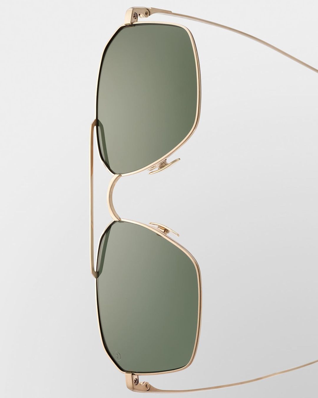 Close-up of gold-rimmed sunglasses with green lenses against a plain white background, showcasing their minimalist design and sleek aesthetic.