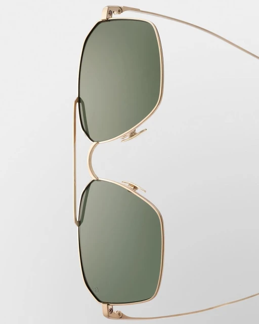 Close-up of gold-rimmed sunglasses with green lenses against a plain white background, showcasing their minimalist design and sleek aesthetic.
