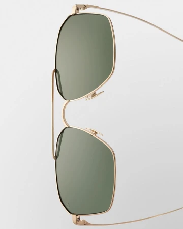 Close-up of gold-rimmed sunglasses with green lenses against a plain white background, showcasing their minimalist design and sleek aesthetic.
