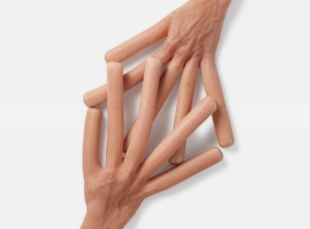 Hands with sausage fingers arranged on a white surface in a studio shot emphasizing humor and surreal food art.