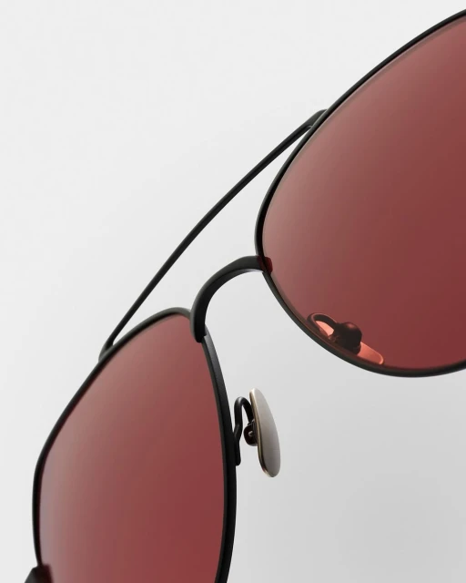 Close-up studio shot of black aviator sunglasses with rose-colored lenses, showcasing the frame details and lens tint against a white backdrop.