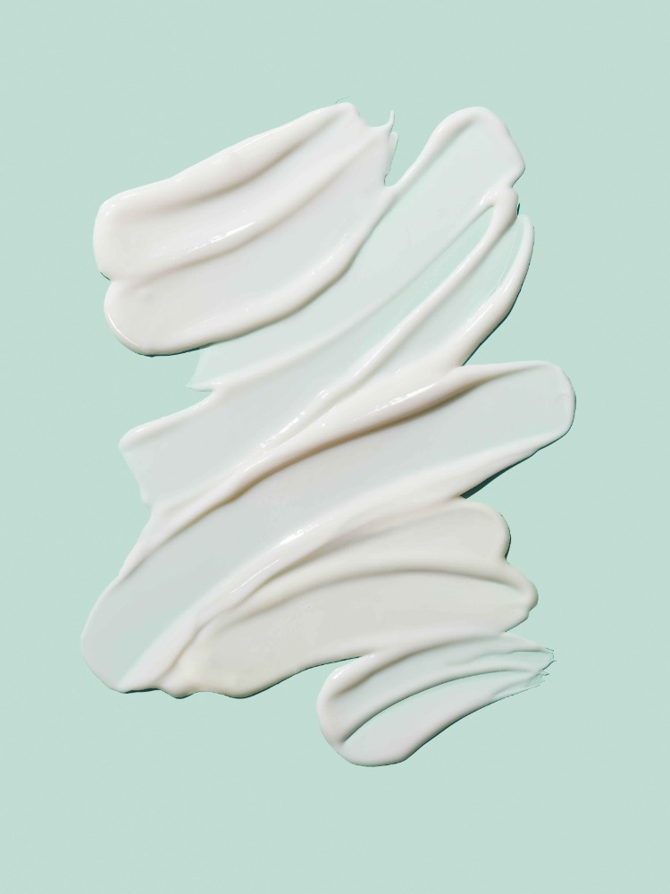 Close-up of thick, creamy white beauty product swirls diagonally across a light blue background, ideal for cosmetic promotions.