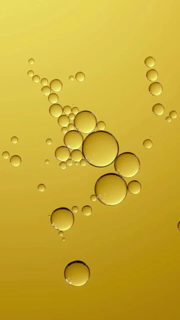 Close-up of golden yellow liquid featuring a collection of transparent spheres, varying in size, against a gradient background.