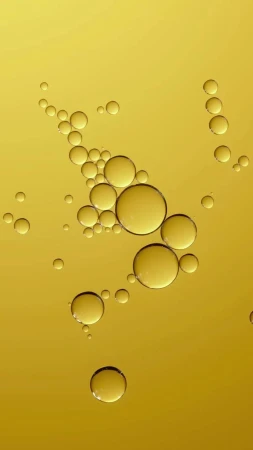 Close-up of golden yellow liquid featuring a collection of transparent spheres, varying in size, against a gradient background.