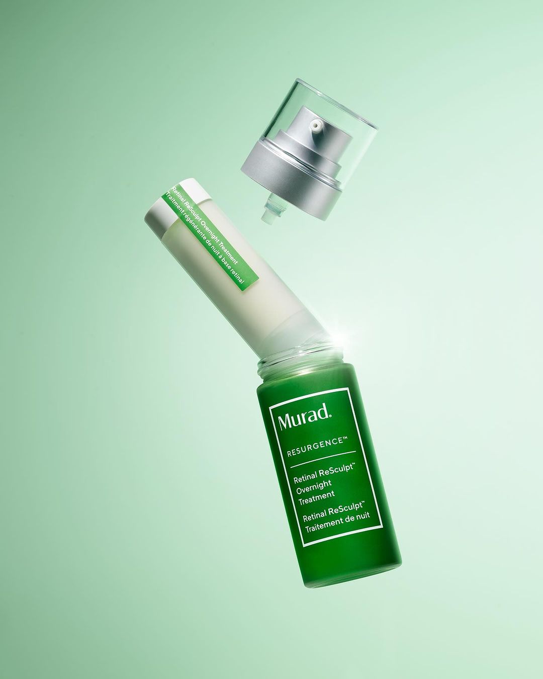 Cosmetic product shot featuring a green glass bottle of Murad Resurgence Retinol ReSculpt Overnight Treatment and its cap, floating.