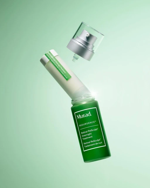Cosmetic product shot featuring a green glass bottle of Murad Resurgence Retinol ReSculpt Overnight Treatment and its cap, floating.