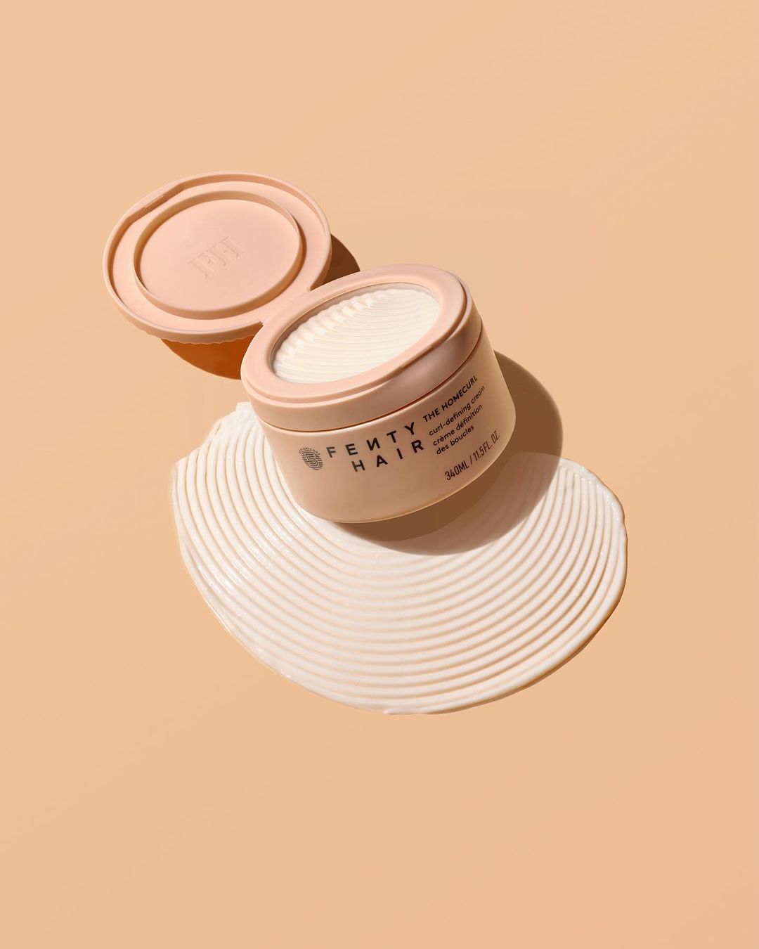 Cosmetic pot from Fenty Hair sitting on swirling creme on peach background in studio shot for beauty and hair care advertising.