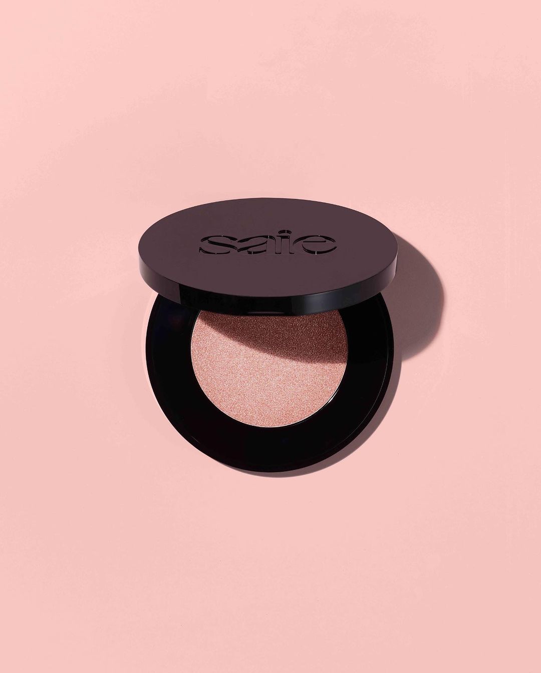 Cosmetic powder in a black compact on a peach background with soft lighting showcases beauty product, simple composition, and clean aesthetic.