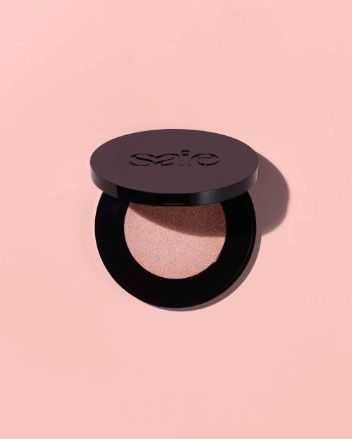 Cosmetic powder in a black compact on a peach background with soft lighting showcases beauty product, simple composition, and clean aesthetic.