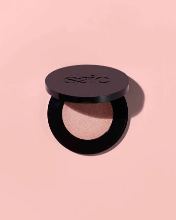 Cosmetic powder in a black compact on a peach background with soft lighting showcases beauty product, simple composition, and clean aesthetic.