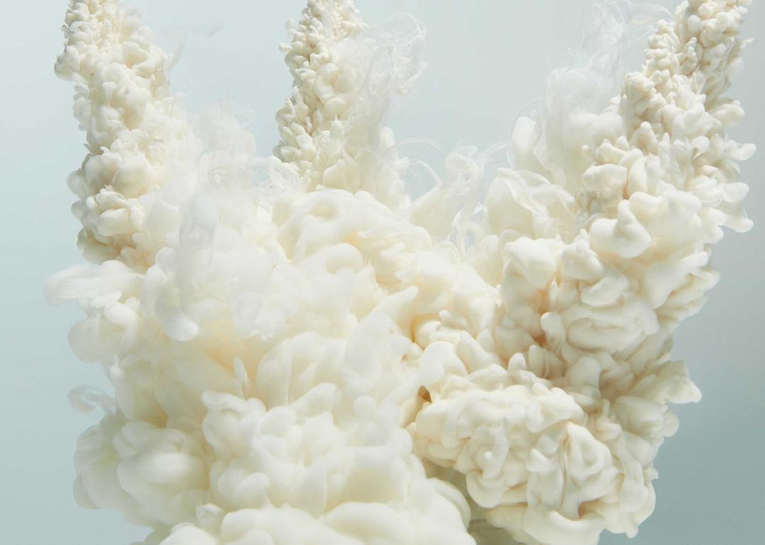 Abstract image featuring swirling white plumes on a soft blue background, resembling smoke or underwater currents in a serene composition.