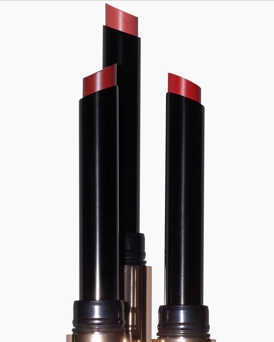 Close-up of three lipstick tubes with red shades against a white background. Beauty product photography.