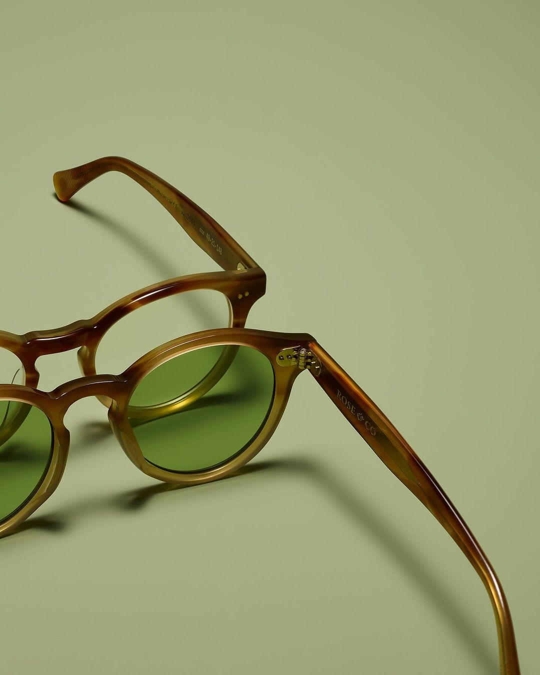 Two pairs of glasses on a light green surface, with one pair featuring green-tinted lenses and brown frames.