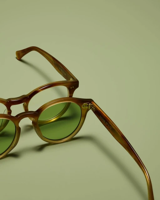 Two pairs of glasses on a light green surface, with one pair featuring green-tinted lenses and brown frames.