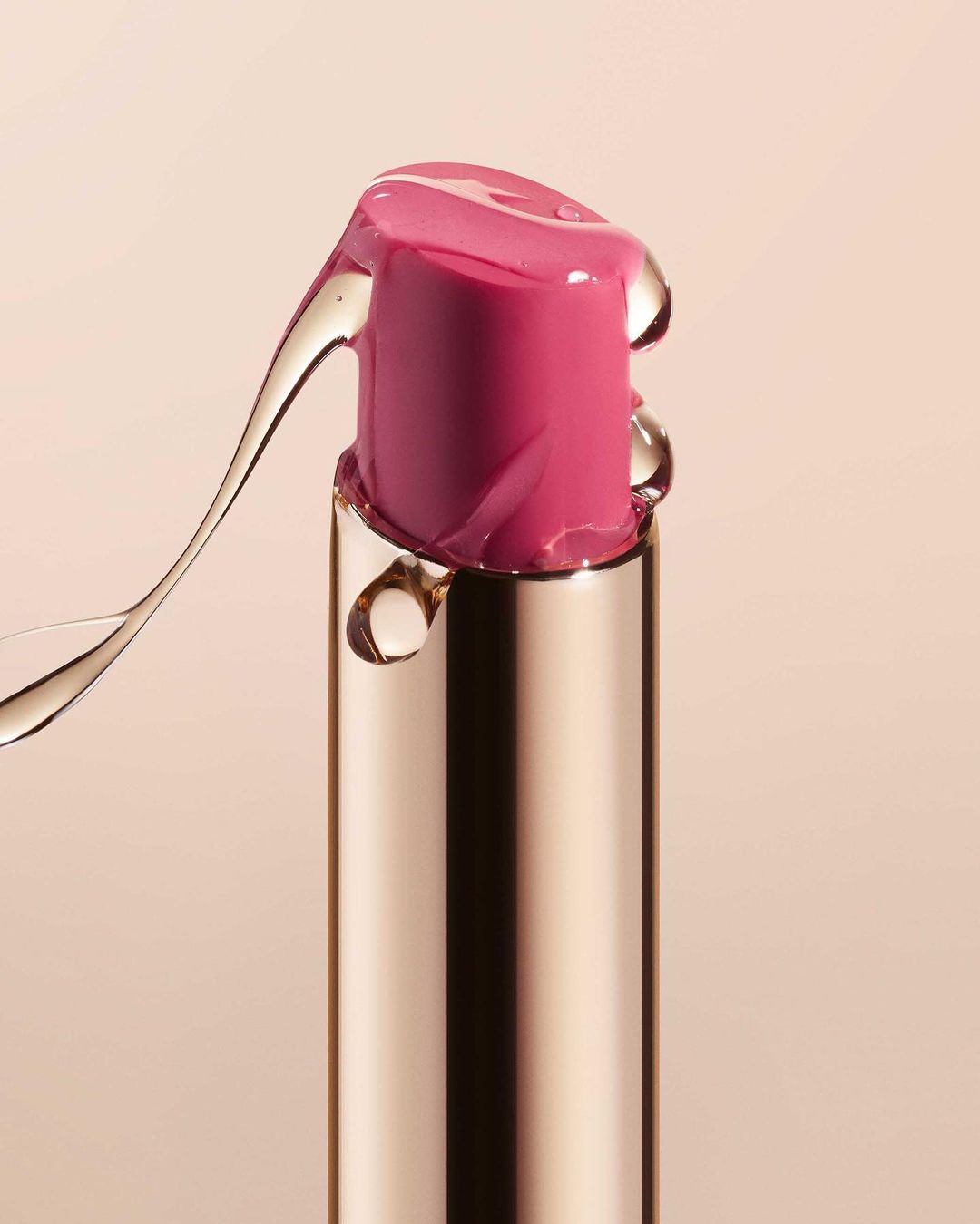 Close-up studio shot of a pink lipstick tube with clear serum dripping down the gold container, showcasing beauty product and textures.