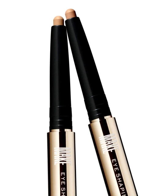 Two Milani Eye Shaping sticks, one tan, one light brown, stand against a white backdrop, creating a beauty product still life.