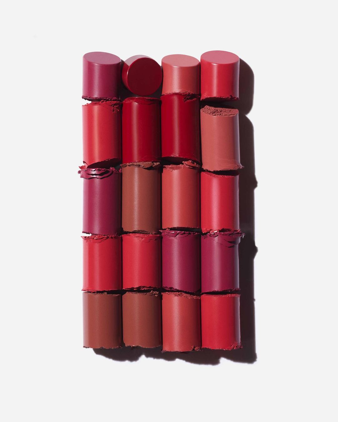 Arrangement of lipstick tubes in various red and pink shades, displayed on a clean white surface. Beauty and cosmetics focus.