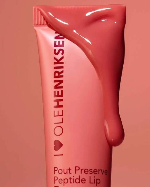 Close-up of pink Ole Henriksen lip treatment tube with product, against a matching pink background. Beauty and skincare product.